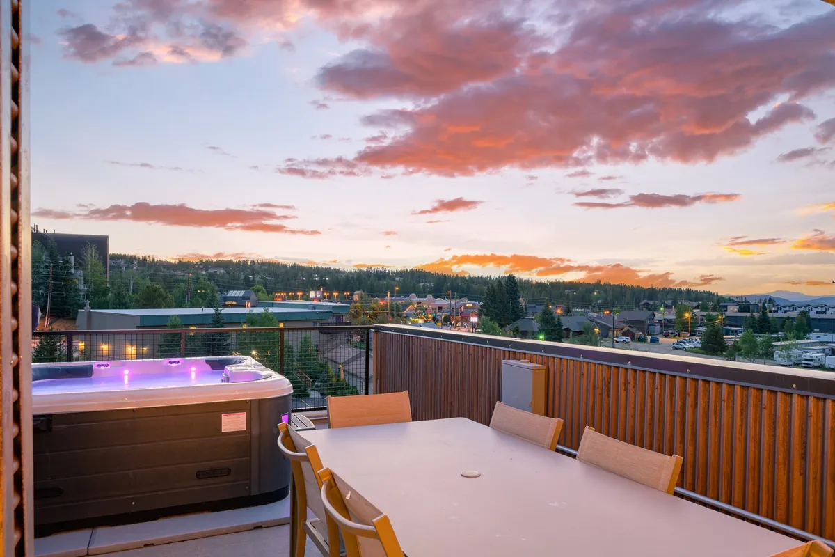 This exterior scene captures a serene hot tub experience with an adjacent outdoor dining table, all set beneath a sunset sky with mountain views. The ambiance is tranquil and invites thoughts of relaxation and stargazing after a day of adventure.