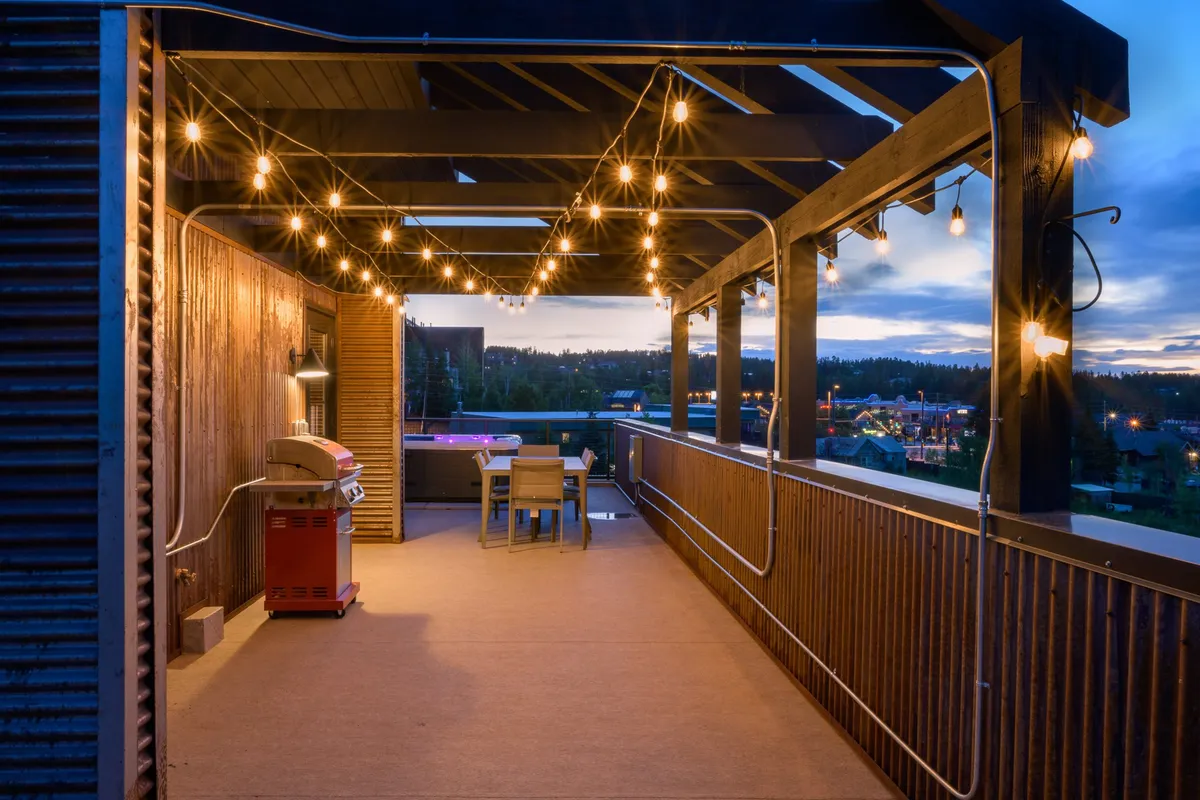 This exterior image captures a rooftop dining area adorned with string lights, a grill, and a large table, perfect for hosting outdoor meals and social gatherings. The warm glow of the lights and the inviting setup create an atmosphere of celebration and togetherness.