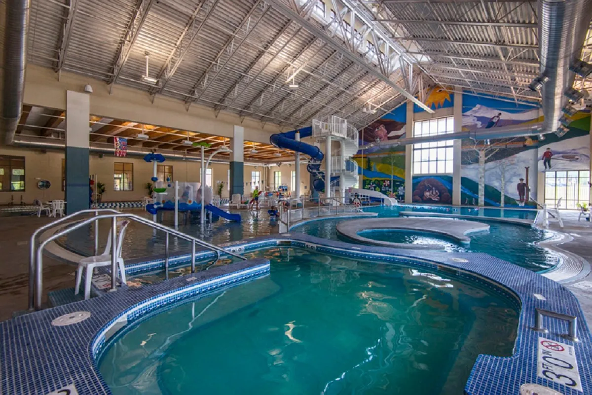 A lively indoor recreation center with water slides, swimming pools, and vibrant murals. Families can be seen swimming, playing, and enjoying the energetic, family-friendly space.