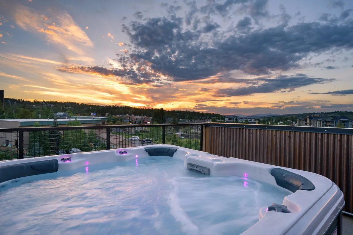 An inviting rooftop hot tub set against a vivid sunset, overlooking the distant landscape. The tranquil water, glowing sky, and open-air setting evoke relaxation after a day of mountain activity.