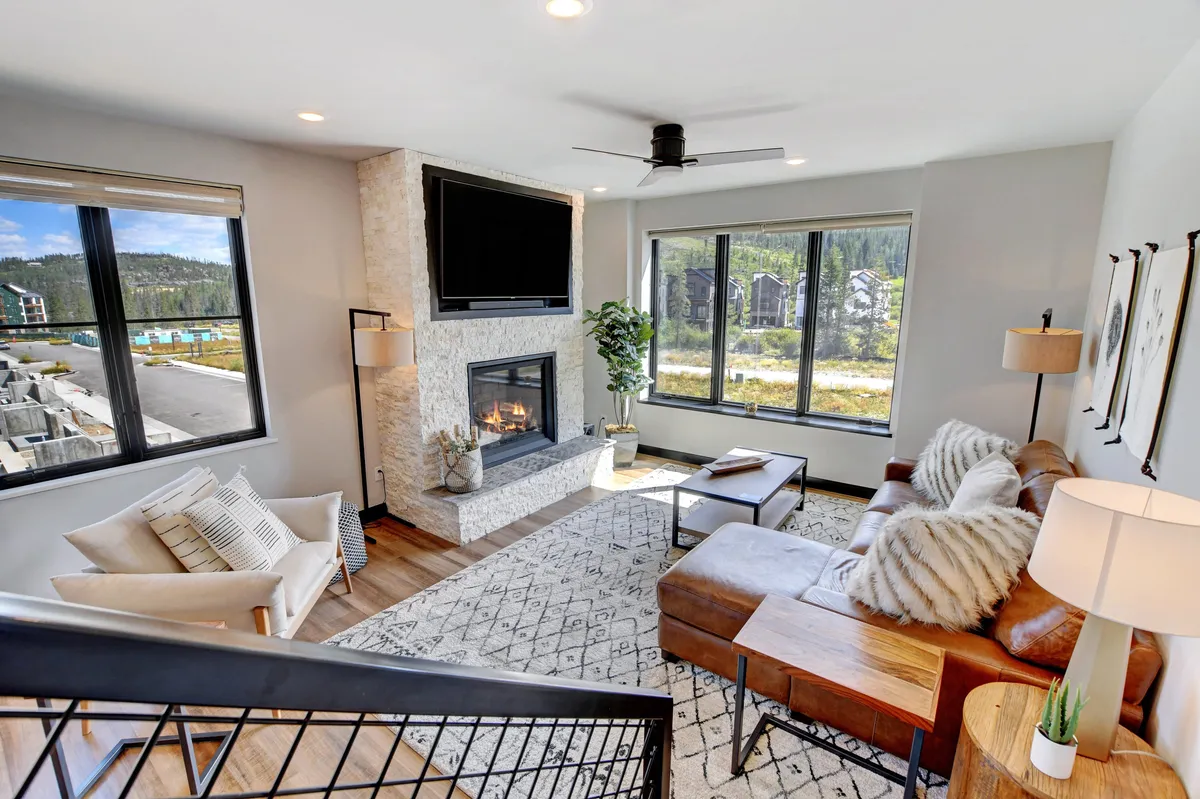 A well-lit living space with a comfortable sofa and a large coffee table arranged around a modern fireplace. Expansive windows provide ample daylight and showcase the beautiful outside scenery. This area is designed for relaxation and informal gatherings, perfectly capturing the ambiance of a shared living zone.