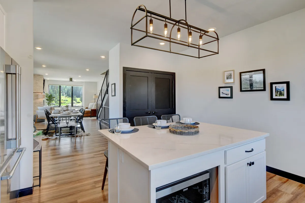A view that seamlessly blends the kitchen island with adjacent dining space, featuring modern lighting, a sleek island countertop, and black doors. The arrangement supports cooking, entertaining, and fluid movement between kitchen and dining.