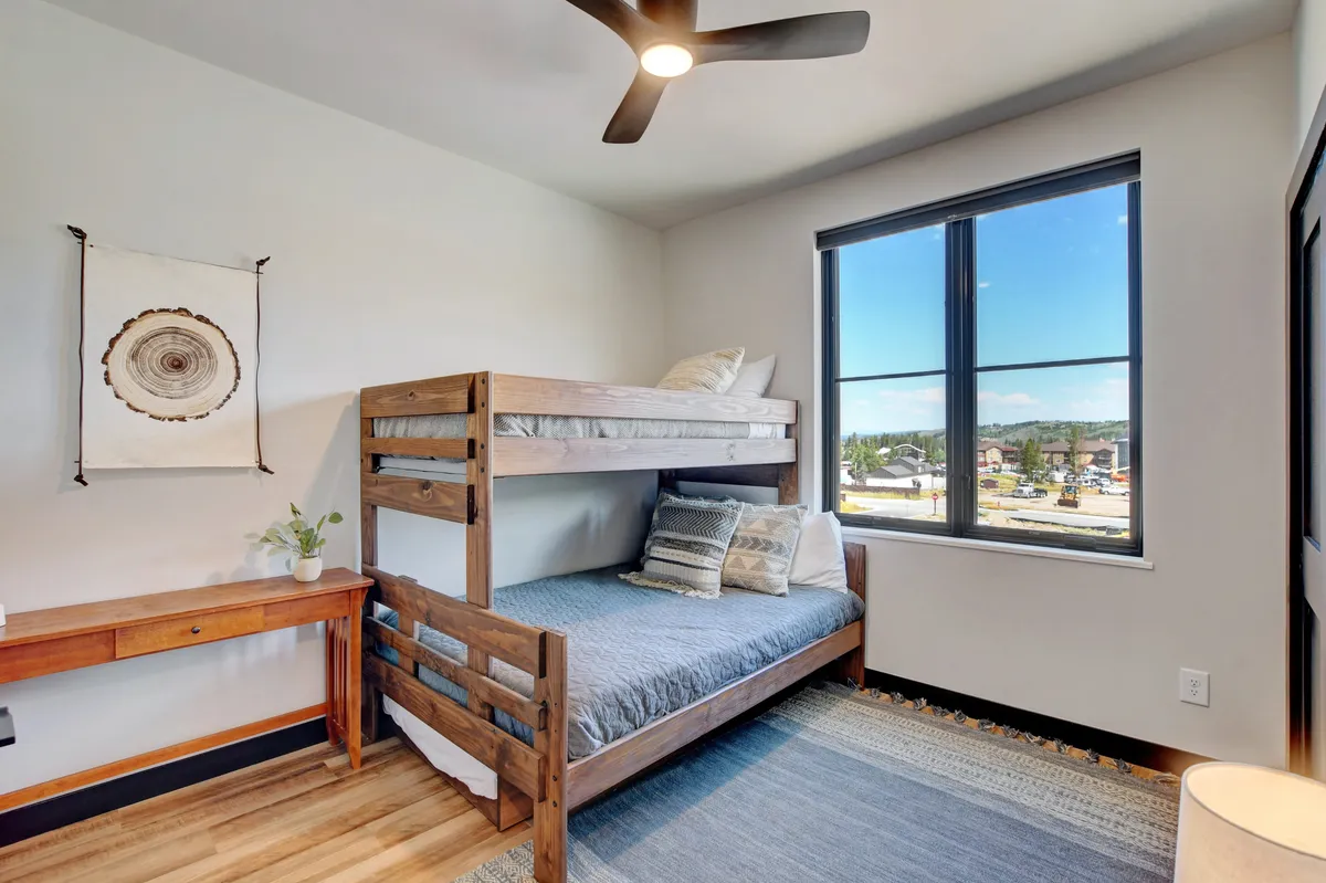A cheerful bunk room with a sturdy wooden bunk bed, an inviting window view, a small desk for activities or games, and playful wall decor. The space radiates a sense of fun and comfort, perfectly suited for families or kids.