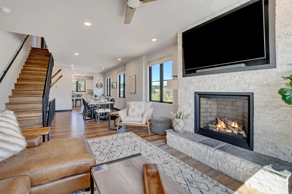 A spacious, sunlit interior with a cozy fireplace, an elegant staircase, a large dining area, and expansive windows. The layout is ideal for gatherings, entertaining, and relaxing after group adventures.