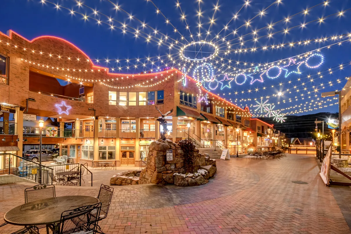 A festive exterior scene featuring decorative lights, star ornaments, a stone fountain, and an outdoor seating area. The setting suggests a vibrant community atmosphere, ideal for holiday events and special evenings out.